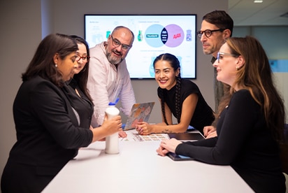 Un equipo trabajando en equipo. Al fondo, un panel interactivo con los logotipos de Palmolive y Ajax